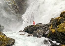 dancer in red standing near waterfall of a norway rocks