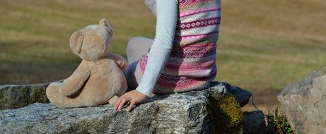 girl with a teddy bear sitting on a stone