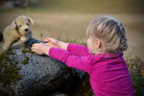 A child plays with a plush toy near a large stone