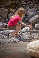 Little blonde girl with long hair by the pond with rocks