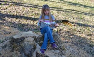 Little girl with a book sitting on a stone