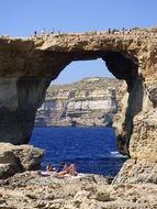 resting humans on the sea bank with rock arch