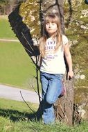 A girl with long hair standing by a tree with her eyes closed