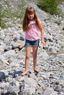 Little girl with long blond hair on the rocks near the pond