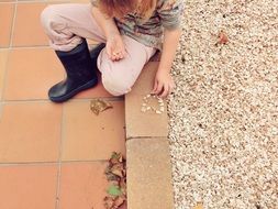 Child is playing with stones near the pavement