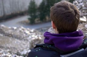 Back view of the boy in winter coat near the water among the trees