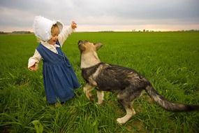 child girl in vintage farm clothes plays with dog on field