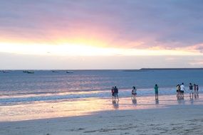 people along the ocean surf at sunset