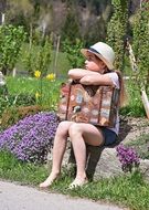 barefoot child girl in hat sits with vintage suitcase in gadren at road