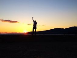 man silhouette with hand up at sunset landscape