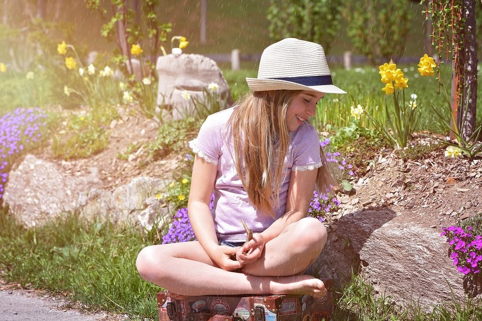 happy barefeet child girl sits on luggage in garden