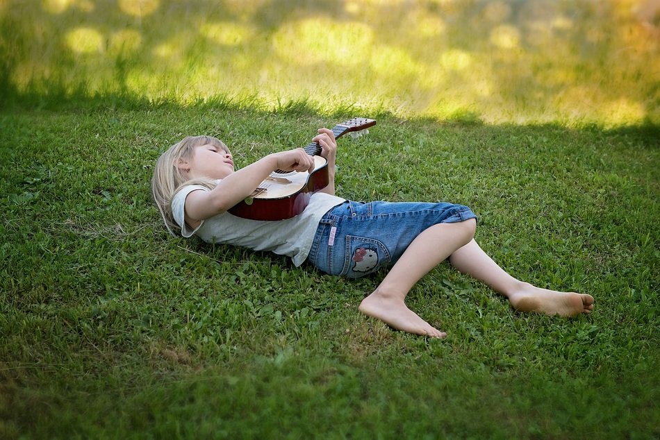 A child with a guitar lies on the grass