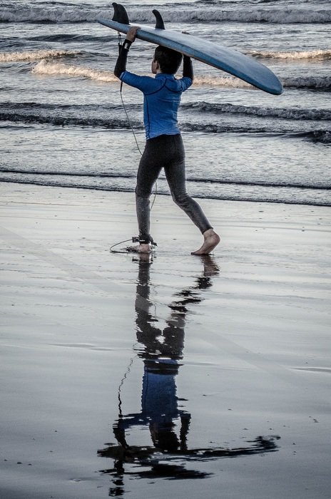 child walking along the beach with a surfboard