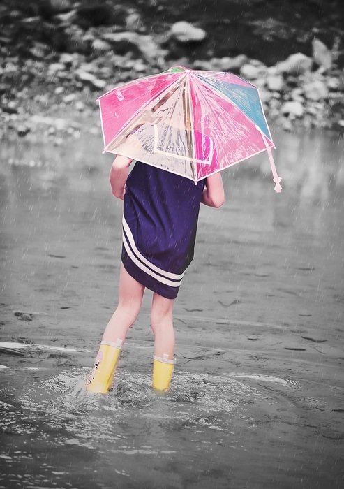 girl in wellies with umbrella walking in water