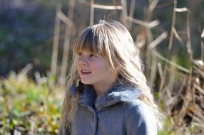 Little girl with long blond hair in a jacket on a sunny day