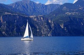 white sailboat in a blue mountain lake in italy