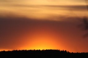 hot colored sunset sky above dark forest