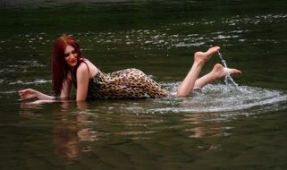 Redhead woman in dress in animal print lying in the water
