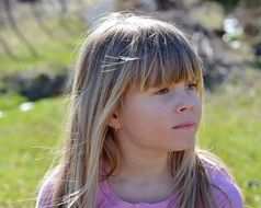 Pensive face of a little girl with long blond hair