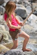 Little girl with long hair with a stick among the stones