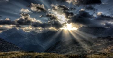 sunlight shining through dark clouds over scenic alps