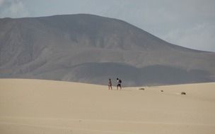 man and woman walking on sand in scenic desert, spain, fuerteventura