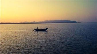 distant view of man in rowing boat on calm water at sunset, france, saint martin