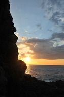 sun sets into ocean behind rock