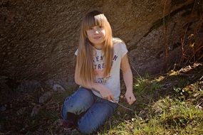 blond girl with long hair near a big stone