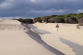 The road among the white sand under storm clouds