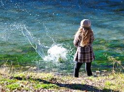 child girl plays on river bank