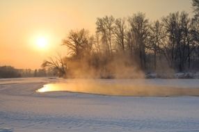 fog above water in front of forest at winter sunset