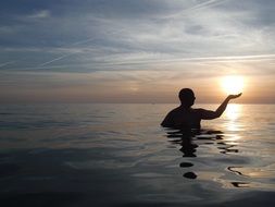 man in sea silhouette with sun on hand