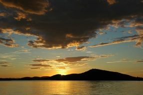 the lake and the distant shore against the backdrop of a cloudy sky at sunset