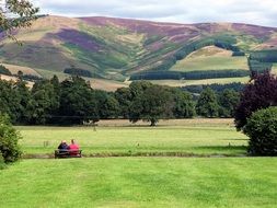 People sit on a wooden bench on a green meadow