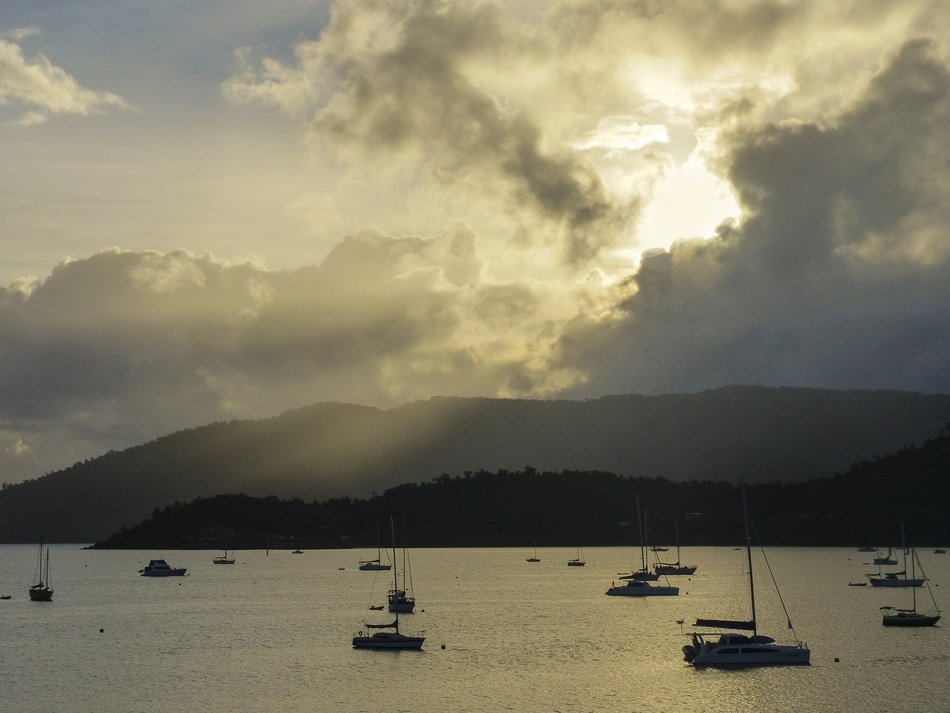 sun in the clouds above the boats on the lake