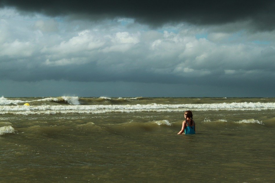 Girl is swimming in the water under the dark clouds