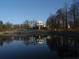 reflection of the sky, trees, and white houses in the pond