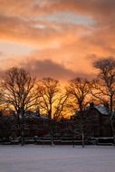 Snow-covered landscape of houses among nature at sunset