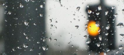 view of a yellow traffic light from a wet window