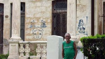 old man smoking in front of old wall with graffiti, cuba, havana