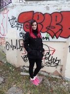 young girl in black clothes posing at wall with red graffiti