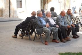 group of old men sitting on benches outdoor, italy