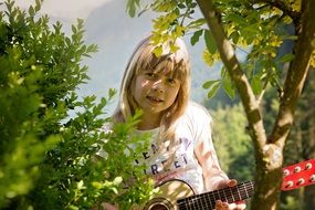 Little girl with a guitar among the trees