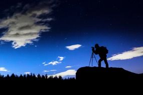 silhouette of photographer on rock above forest, digital art