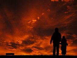 silhouettes of an adult and a child against the backdrop of a fiery sunset