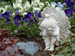 figure of a white mourning angel among flowers in a graveyard