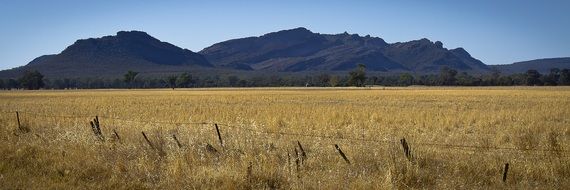 fenced harvested field in front of distant mountains, australia, victoria, grampians