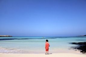 Child standing on a beautiful white sand beach at blue sky