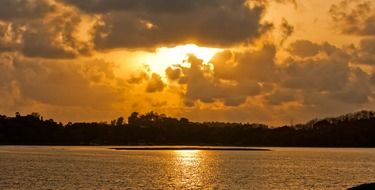 Beautiful lake landscape among the trees with colorful sunset in the clouds